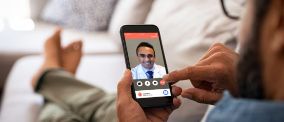 Closeup of a man hand holding cellphone with internet browser on screen. Man with spectacles relaxing sitting on couch while looking at mobile phone. Closeup of mature latin man using smartphone to checking email at home.