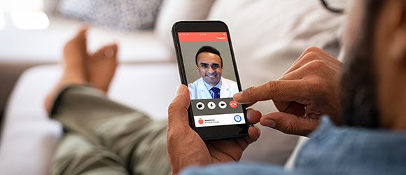 Closeup of a man hand holding cellphone with internet browser on screen. Man with spectacles relaxing sitting on couch while looking at mobile phone. Closeup of mature latin man using smartphone to checking email at home.