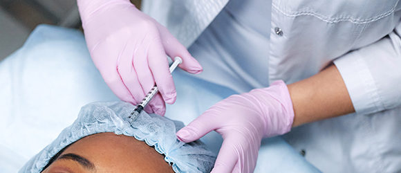 Woman receiving neurotoxin injections via needle in forehead